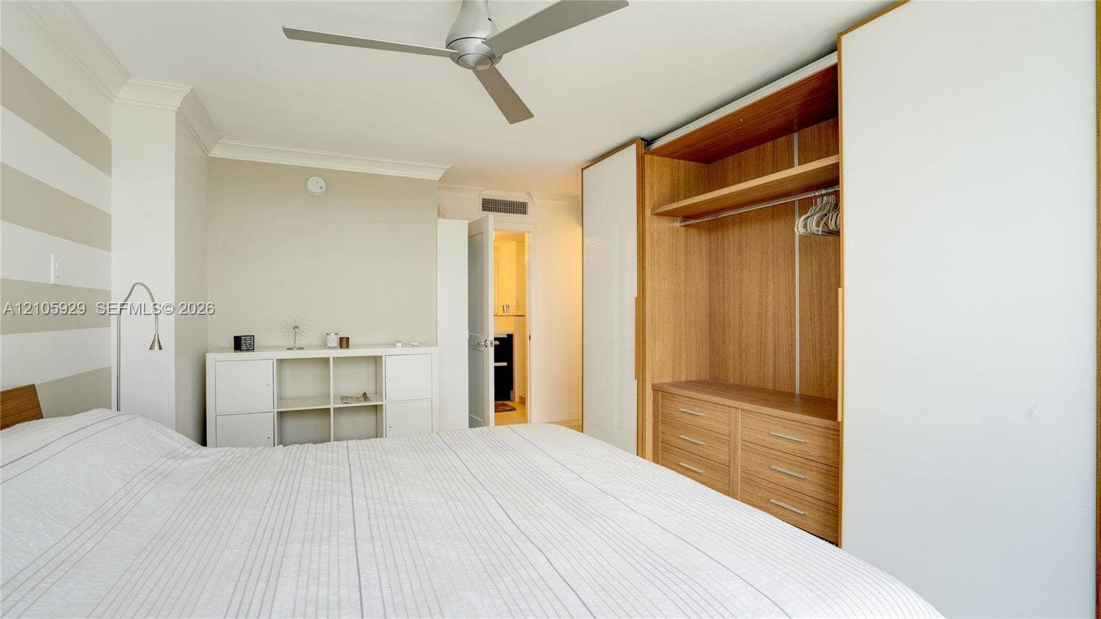 2655 Collins Avenue, #2301, Miami Beach, FL 33140 Built-in floor-to-ceiling wardrobe with sliding white panels, wood-finish interior shelving, and integrated drawers, featuring a modern three-blade ceiling fan and crown molding