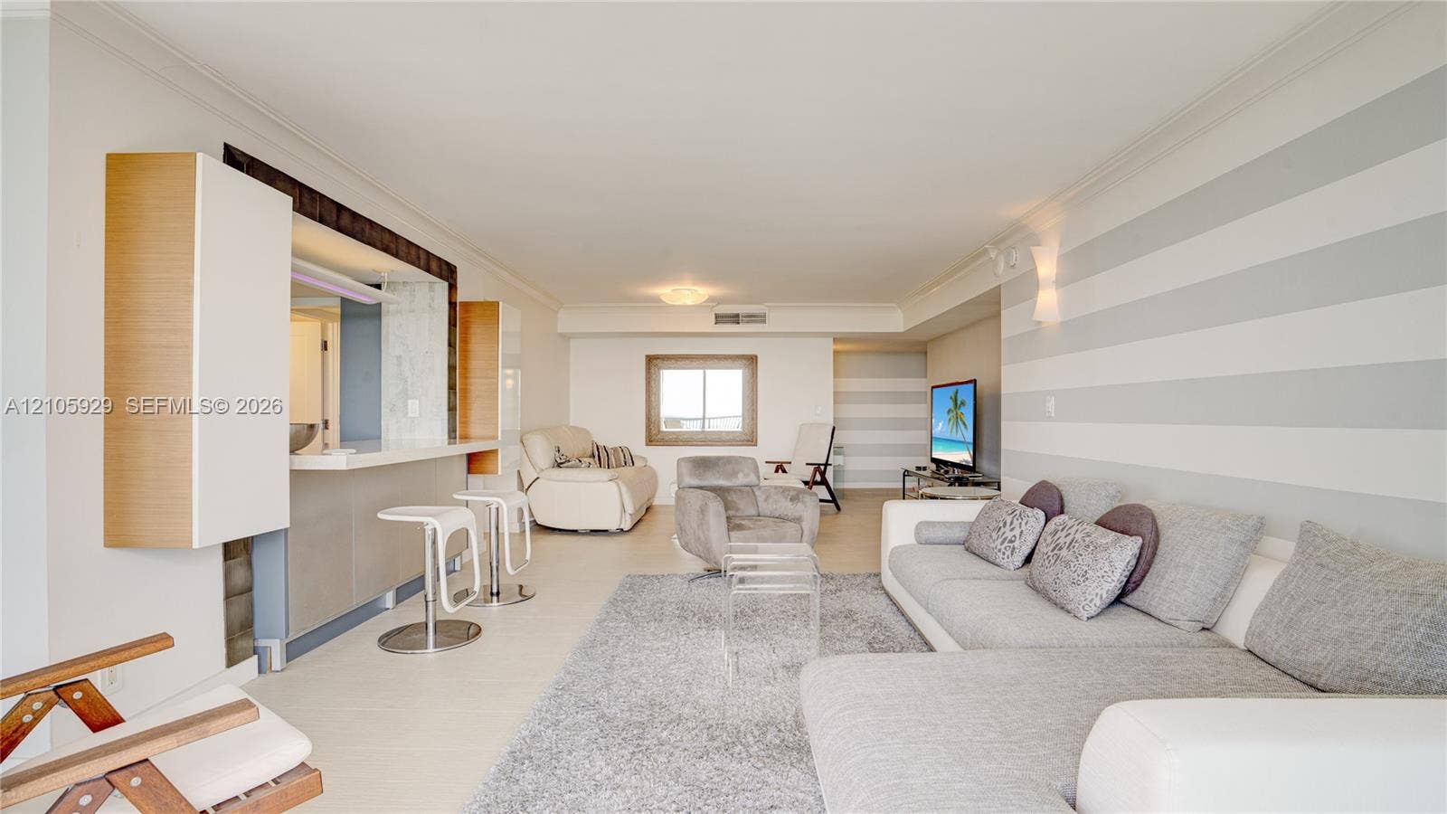 2655 Collins Avenue, #2301, Miami Beach, FL 33140 Living area featuring a service pass-through with a breakfast bar, neutral-tone striped wall treatments, crown molding, and large-format tile flooring