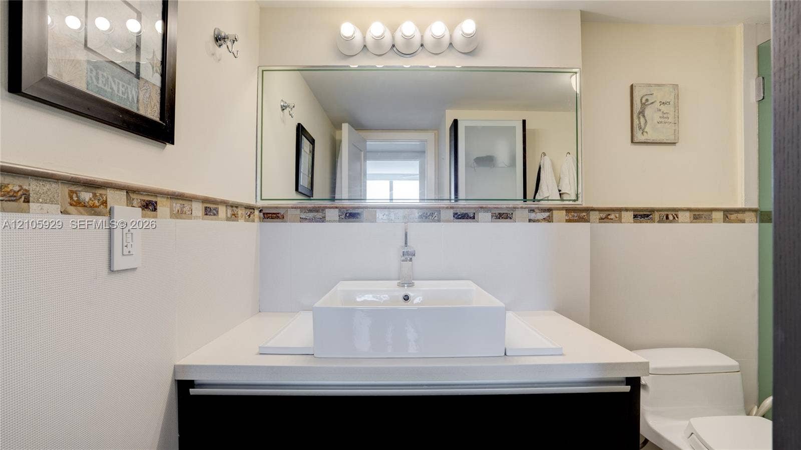 2655 Collins Avenue, #2301, Miami Beach, FL 33140 Vanity featuring a rectangular vessel sink, solid-surface countertop, decorative tile backsplash, wall-mounted mirror, and multi-bulb light fixture