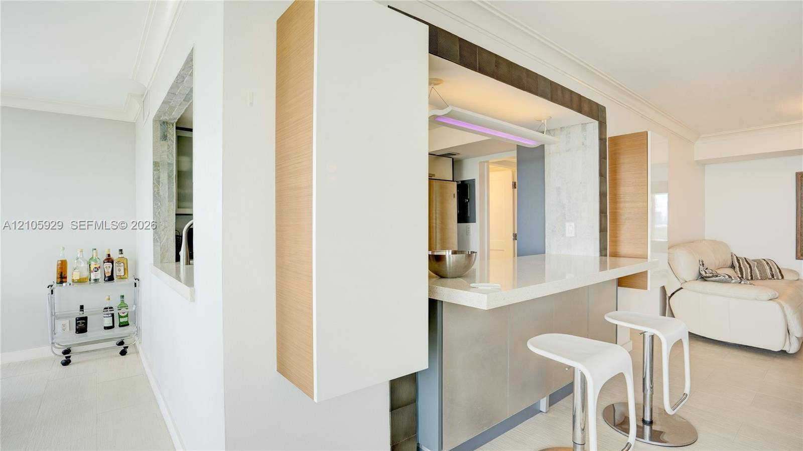 2655 Collins Avenue, #2301, Miami Beach, FL 33140 Kitchen featuring a quartz countertop breakfast bar, custom light-toned wood cabinetry, stone-tile backsplash, and tiled flooring