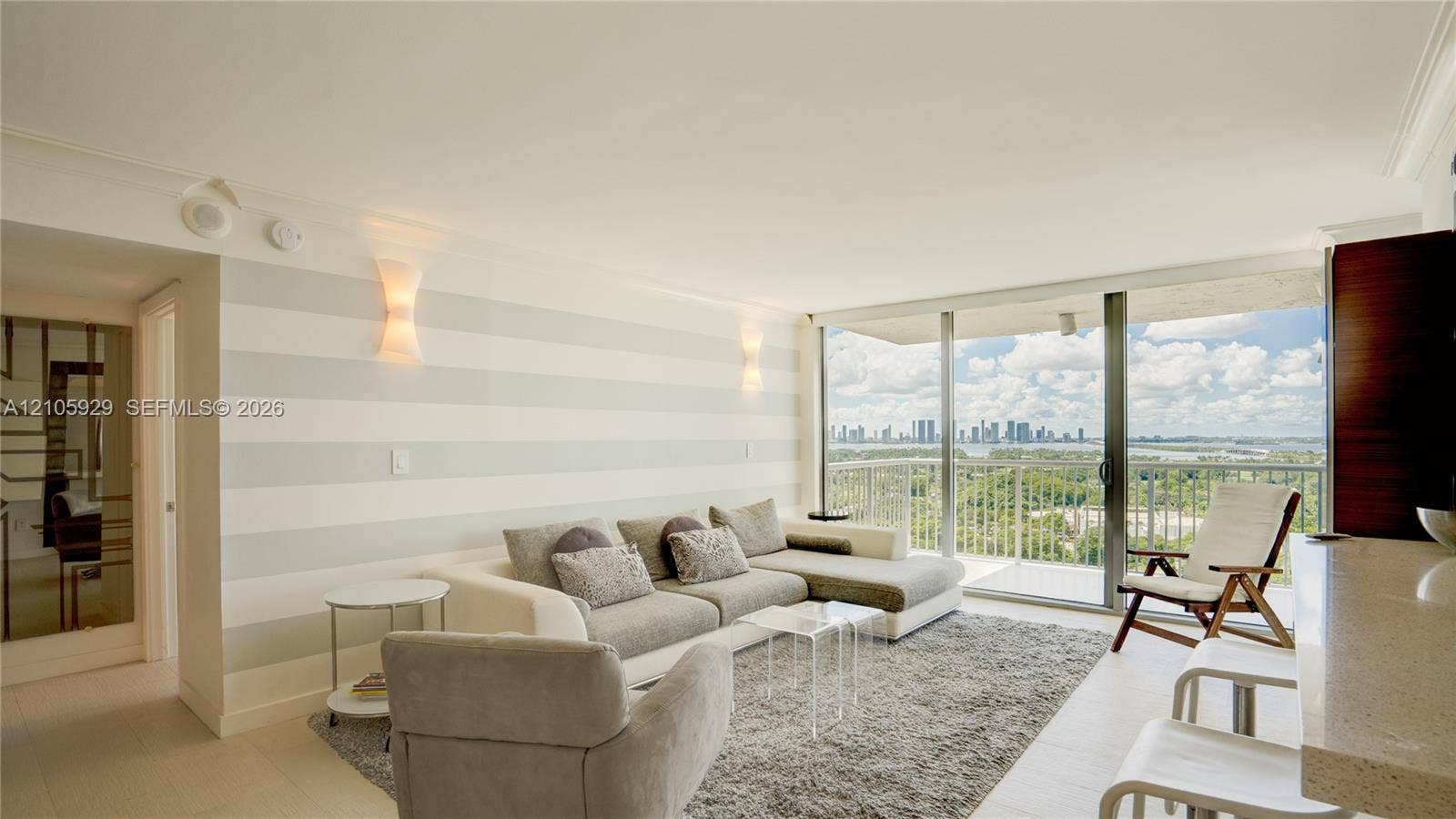 2655 Collins Avenue, #2301, Miami Beach, FL 33140 Floor-to-ceiling sliding glass doors, private balcony, neutral-toned striped accent wall, integrated wall sconce lighting, and light-toned tile flooring