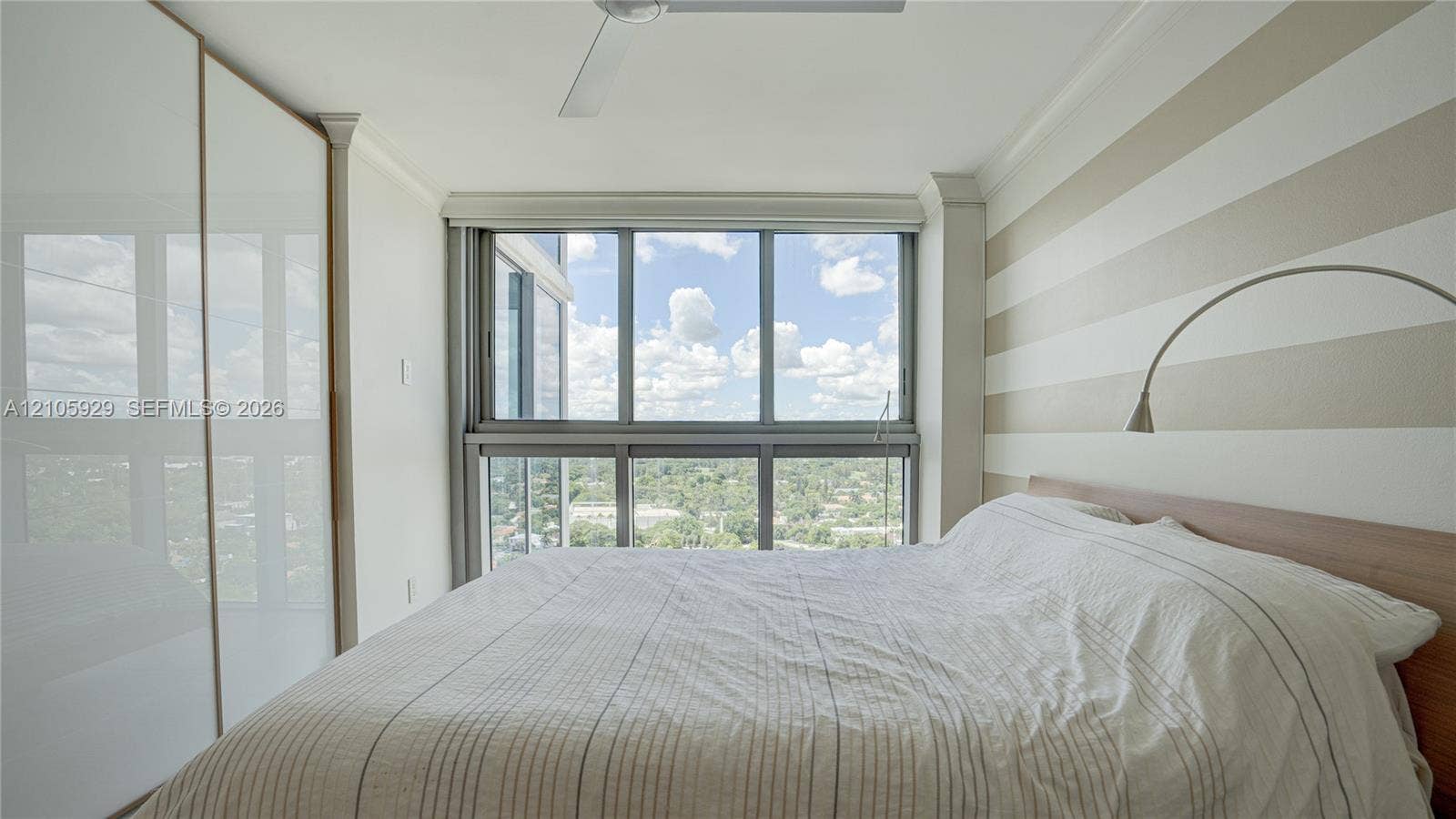2655 Collins Avenue, #2301, Miami Beach, FL 33140 Floor-to-ceiling windows, high-gloss white built-in wardrobe, ceiling-mounted fan, and wall-mounted articulating light fixture