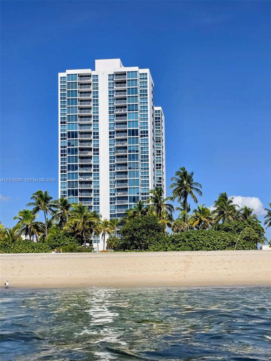 2655 Collins Avenue, #2301, Miami Beach, FL 33140 High-rise residential tower featuring a glass facade, private balconies, and direct beachfront access, surrounded by mature palm trees- view from the ocean