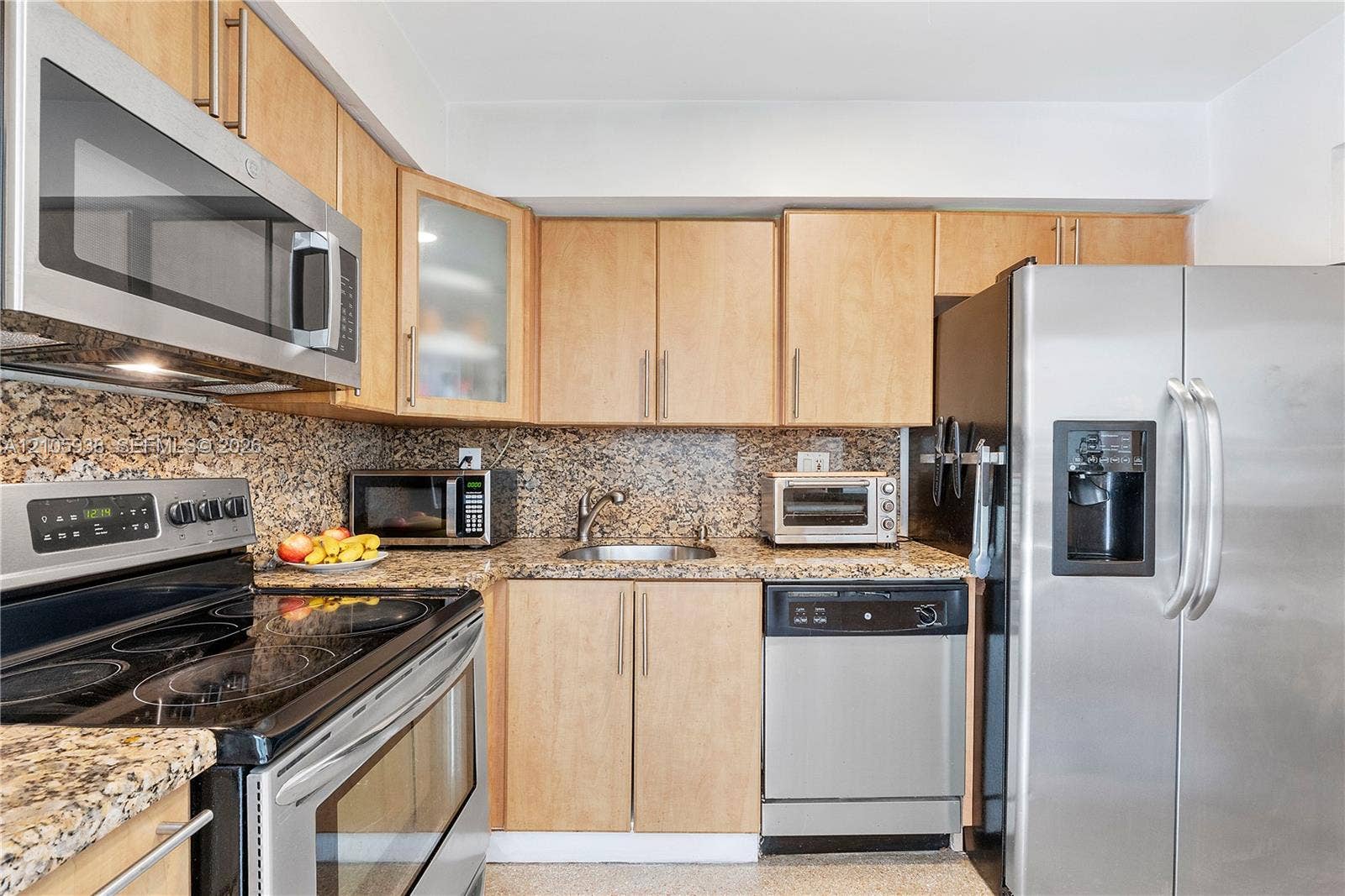 8310 NW 10th Street, Pembroke Pines, FL 33024 Kitchen featuring light-wood cabinetry, stone countertops, integrated stainless steel appliances, and a glass-paneled upper cabinet
