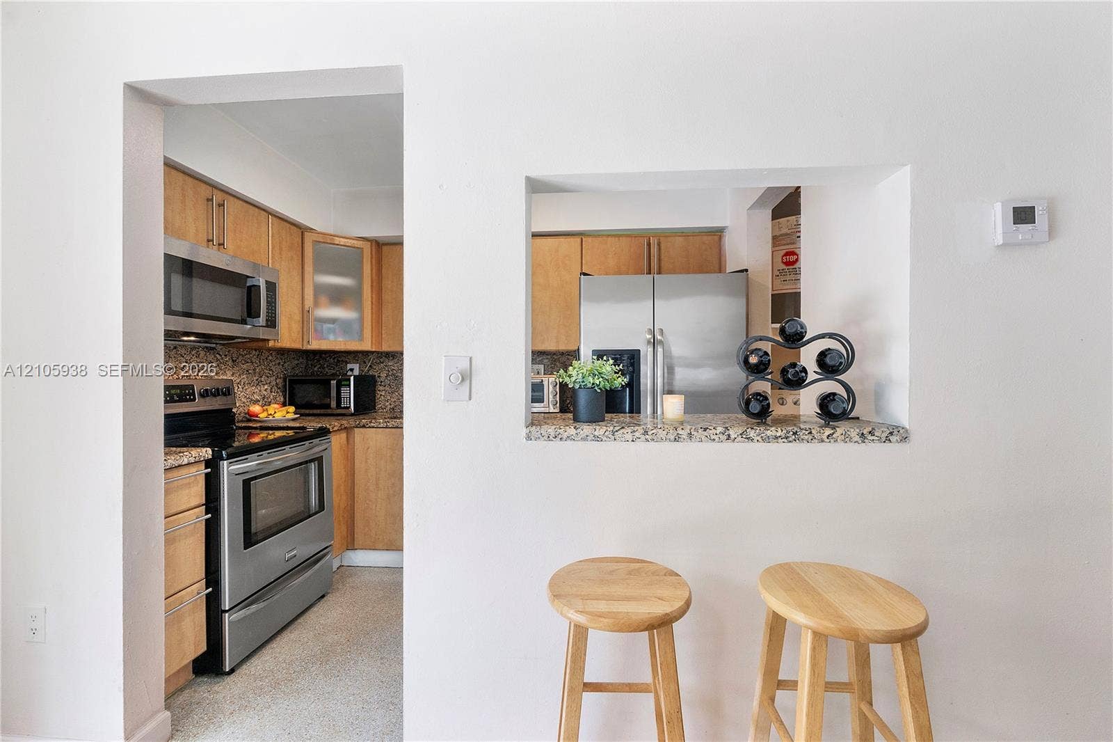 8310 NW 10th Street, Pembroke Pines, FL 33024 Kitchen featuring wood cabinetry, stone-finish countertops, stainless steel appliances, and a pass-through opening with a breakfast bar