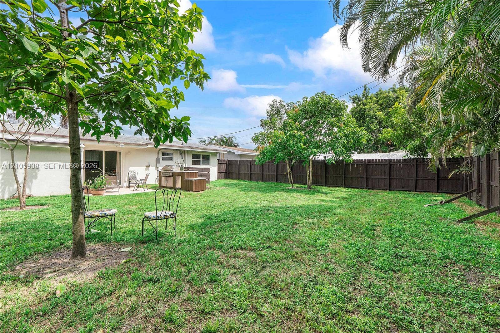 8310 NW 10th Street, Pembroke Pines, FL 33024 Backyard featuring a grass lawn, mature trees, wood privacy fencing, and a concrete patio