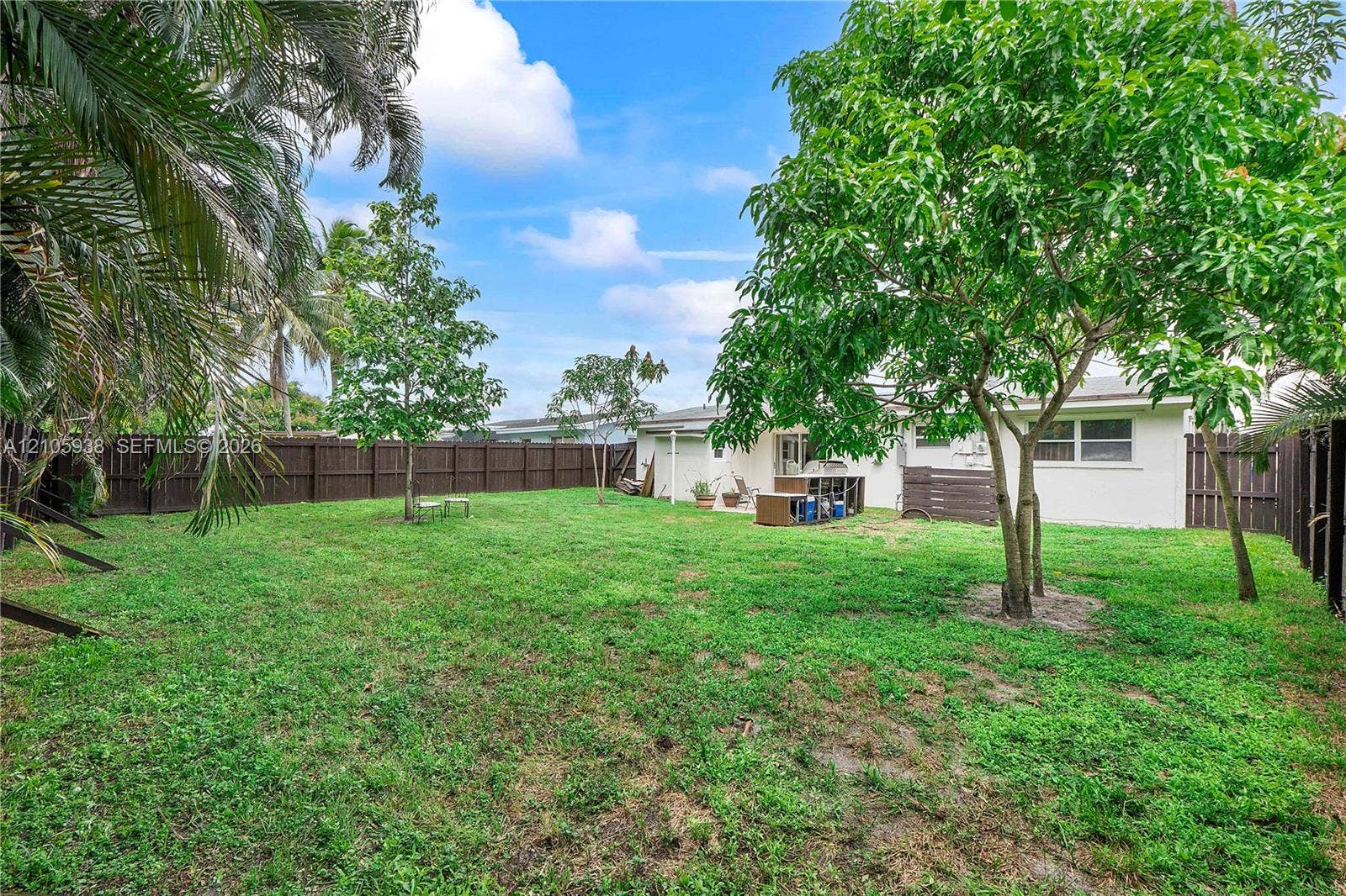8310 NW 10th Street, Pembroke Pines, FL 33024 Expansive backyard featuring a large grass lawn, perimeter wood privacy fencing, mature trees, and palm foliage