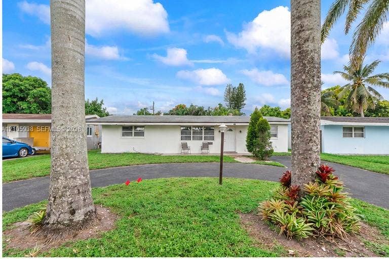 8310 NW 10th Street, Pembroke Pines, FL 33024 Single-story residence featuring a stucco exterior, a curved asphalt driveway, and mature palm trees
