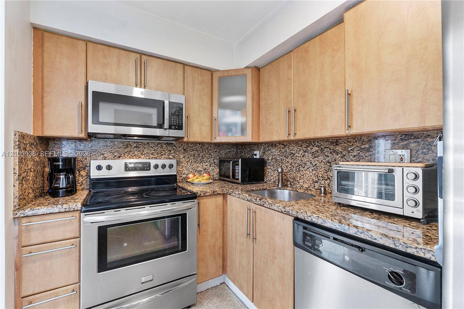 8310 NW 10th Street, Pembroke Pines, FL 33024 Kitchen featuring light-finish cabinetry with vertical hardware, stone-patterned countertops, stainless steel appliances, and a glass-paneled upper cabinet door