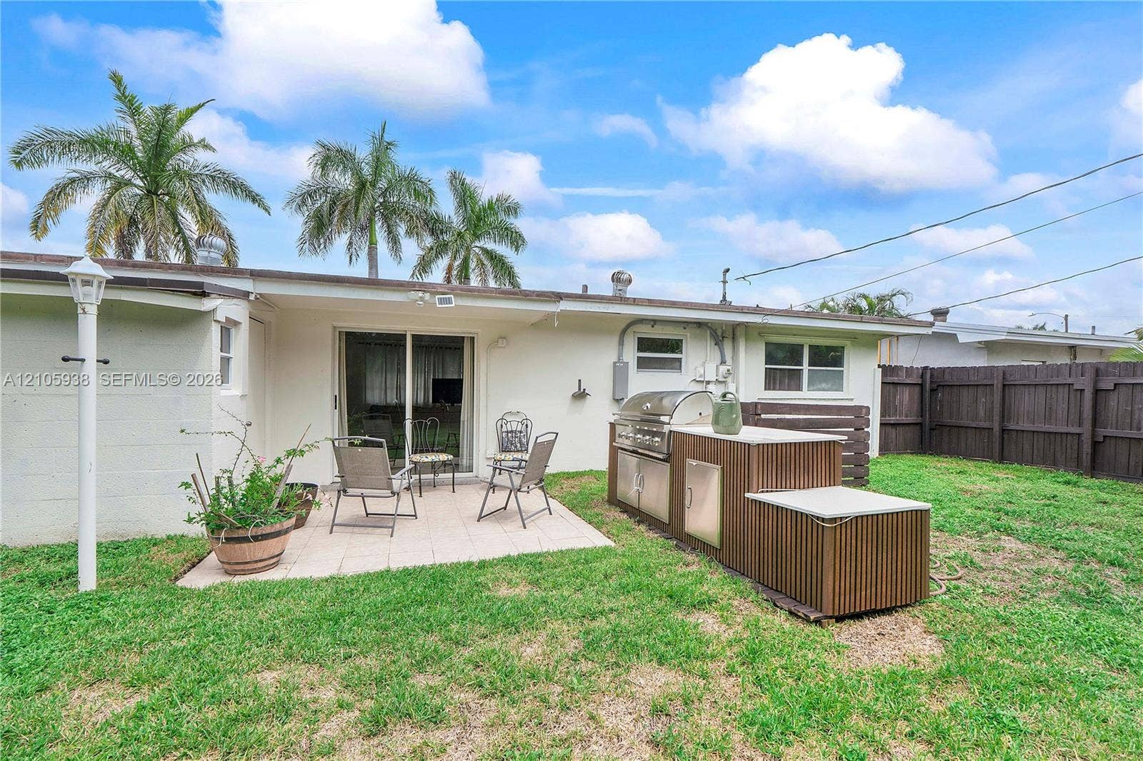 8310 NW 10th Street, Pembroke Pines, FL 33024 Backyard featuring a paved patio, a built-in outdoor kitchen with a stainless steel grill, a vertical wood-slat island base, and a perimeter privacy fence