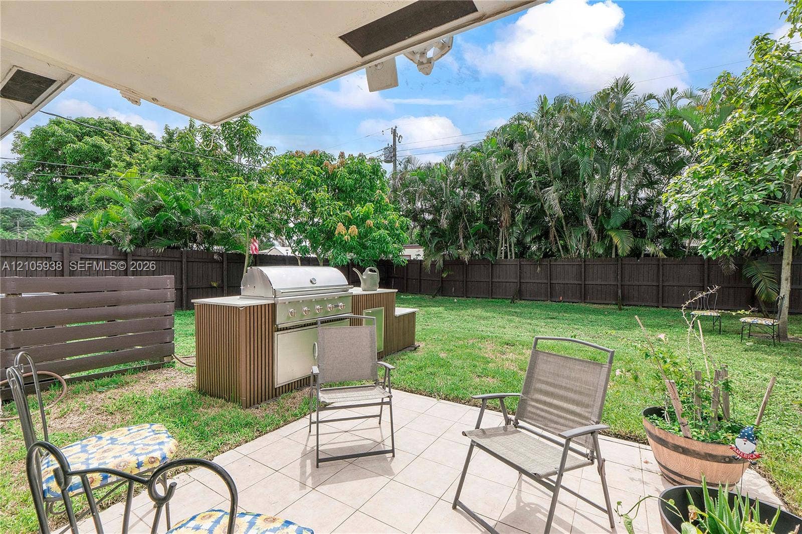 8310 NW 10th Street, Pembroke Pines, FL 33024 Covered patio featuring ceramic tile flooring, built-in outdoor kitchen with stainless steel grill, and enclosed backyard with perimeter fencing