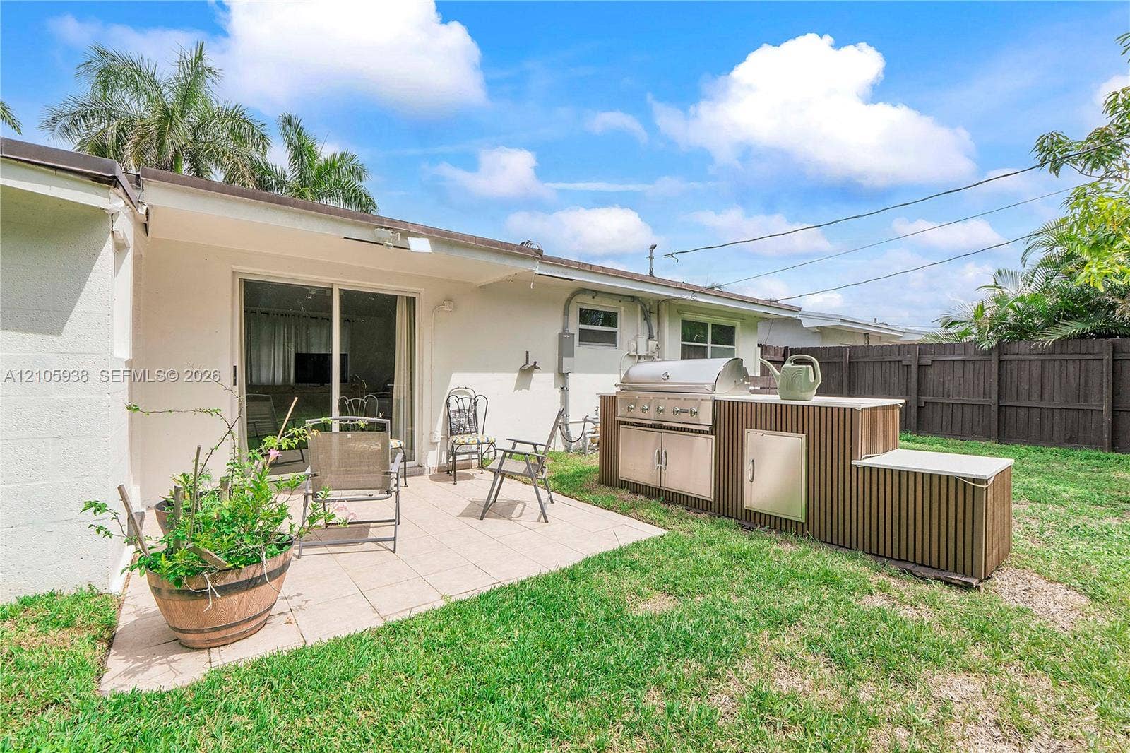 8310 NW 10th Street, Pembroke Pines, FL 33024 Outdoor patio with tile flooring and a built-in outdoor kitchen featuring a stainless steel grill, cabinetry, and a stone-finish countertop, all enclosed by a wooden privacy fence