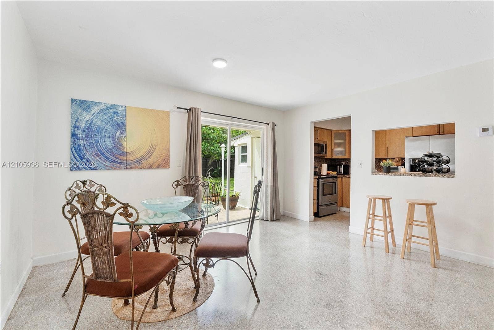 8310 NW 10th Street, Pembroke Pines, FL 33024 Neutral-toned interior space featuring polished concrete flooring, a sliding glass door providing exterior access, and a kitchen pass-through window with a countertop ledge
