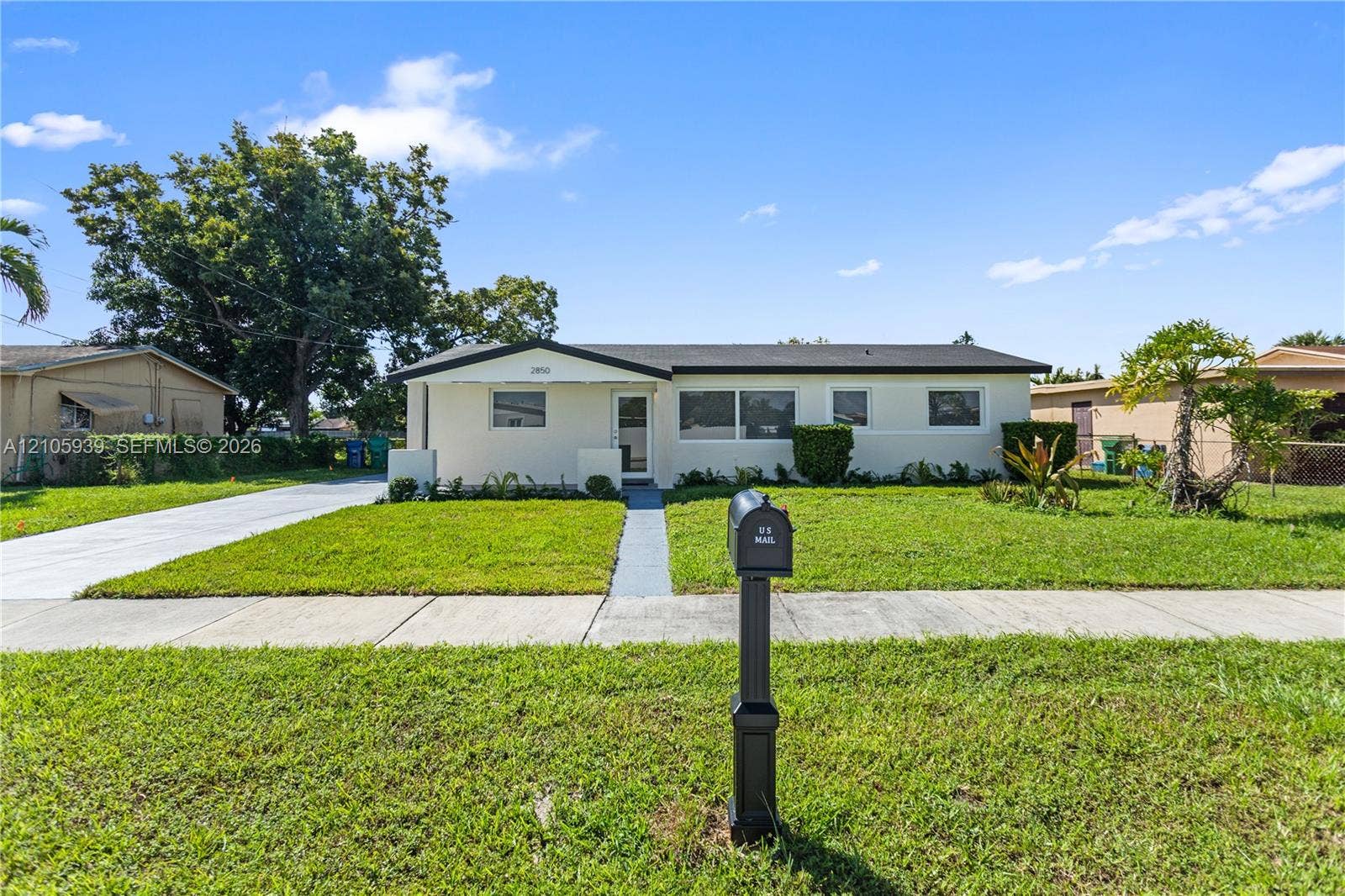 2850 NW 205th Street, Miami Gardens, FL 33056 Single-story exterior featuring a light-colored stucco facade, a low-pitched roofline, a paved driveway, and an expansive front lawn