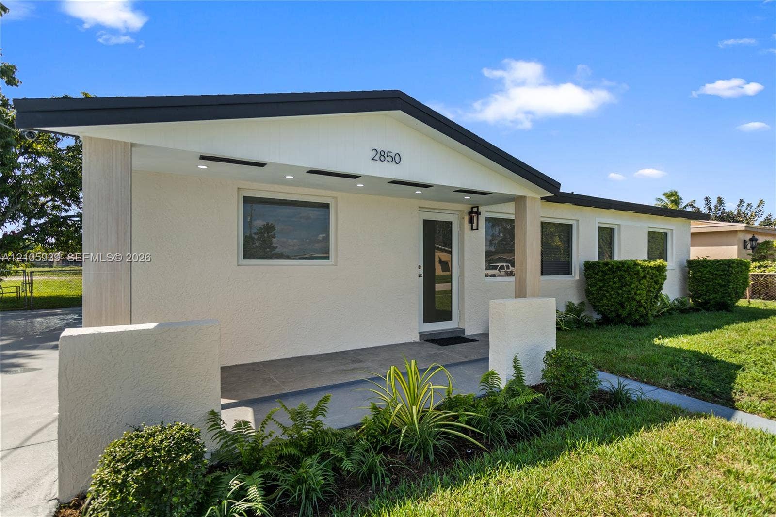2850 NW 205th Street, Miami Gardens, FL 33056 Single-story exterior featuring a textured stucco facade, covered porch with recessed lighting, and architectural gable roofline
