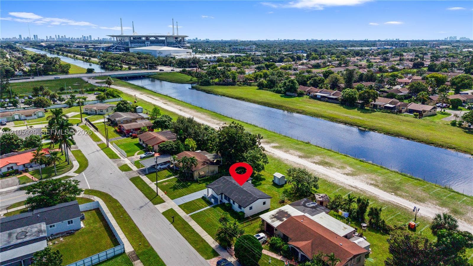 2850 NW 205th Street, Miami Gardens, FL 33056 Aerial perspective of a detached single-story residence situated along a canal-front lot, featuring a shingled roof, concrete driveway, and established lawn
