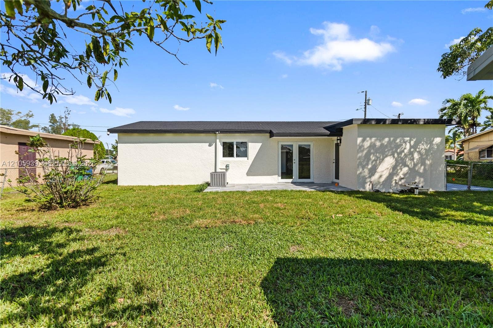 2850 NW 205th Street, Miami Gardens, FL 33056 Exterior elevation featuring a light-colored stucco finish, dark-toned roofline, glass-paneled double doors, and an expansive rear lawn