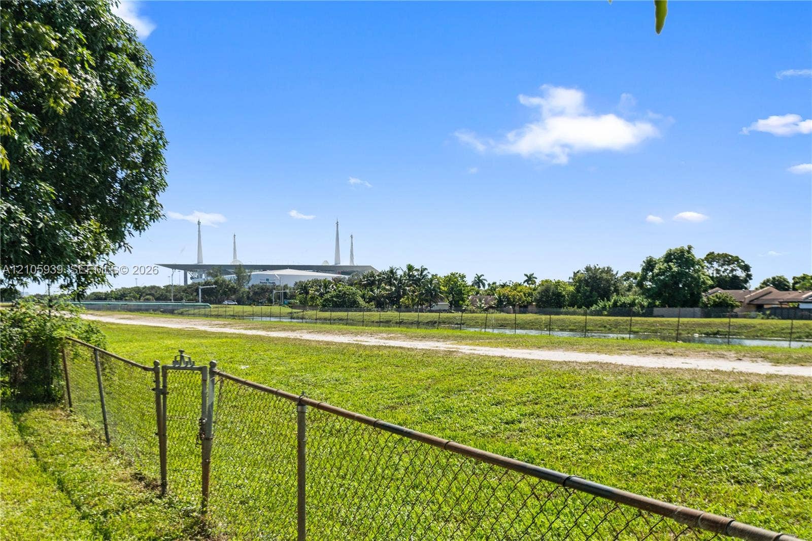 2850 NW 205th Street, Miami Gardens, FL 33056 Expansive grassy lot enclosed by a chain-link fence, featuring open terrain, mature perimeter trees, and a waterway border