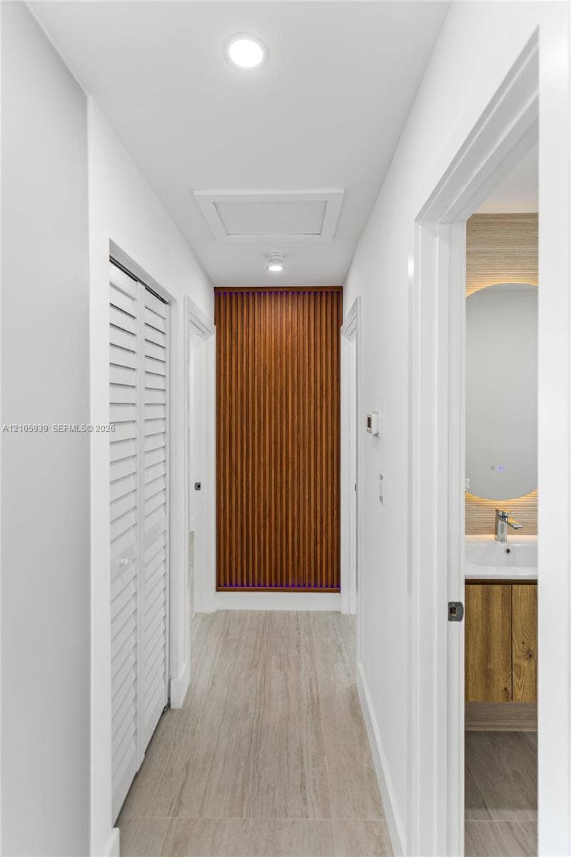 2850 NW 205th Street, Miami Gardens, FL 33056 Hallway featuring wood-slat accent wall, white louvered closet doors, recessed lighting, and wood-finish flooring