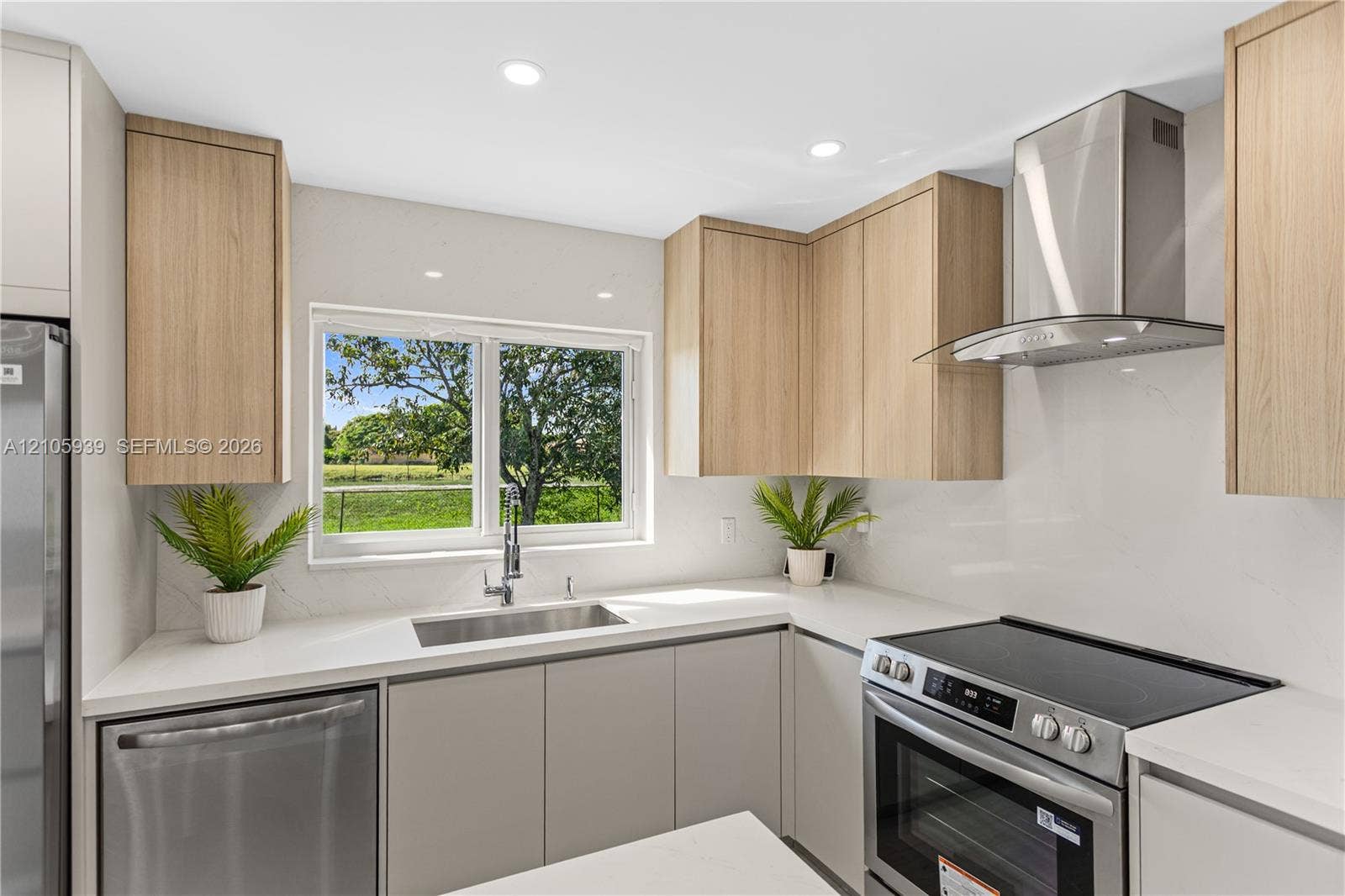2850 NW 205th Street, Miami Gardens, FL 33056 Kitchen featuring light wood-finish cabinetry, stainless steel appliances, solid-surface countertops, a stainless steel undermount sink, and an integrated stainless steel range hood