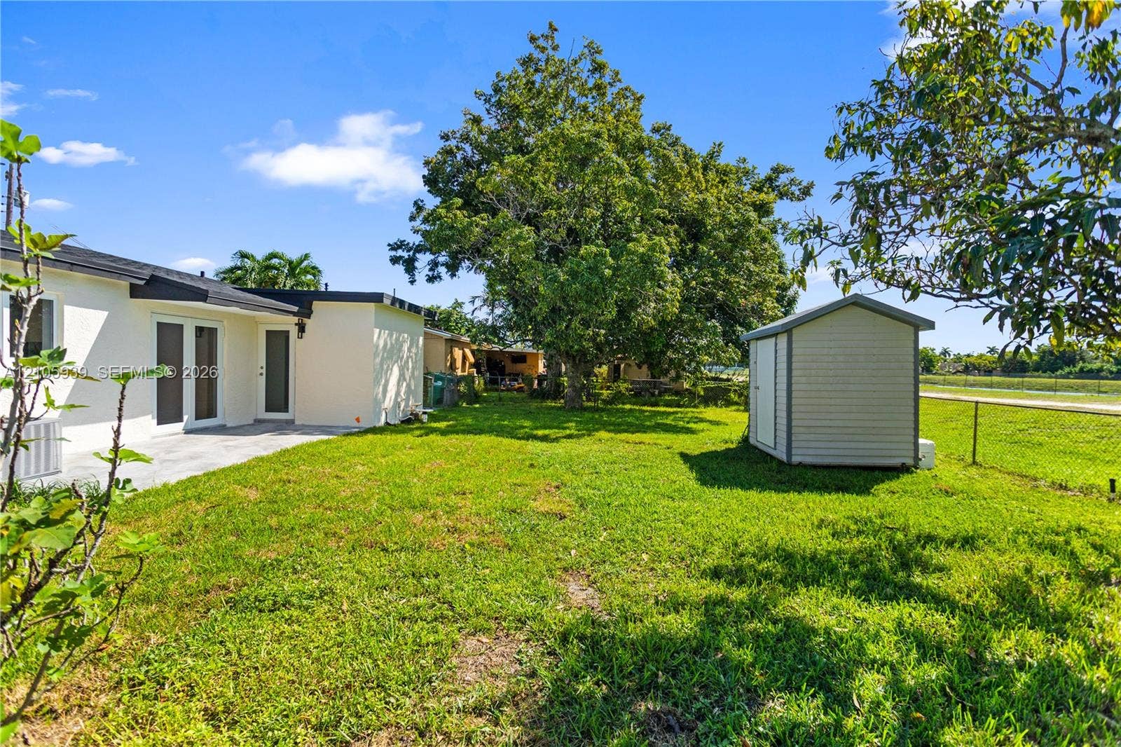 2850 NW 205th Street, Miami Gardens, FL 33056 Backyard featuring a concrete patio, freestanding storage shed, established trees, and chain-link fencing