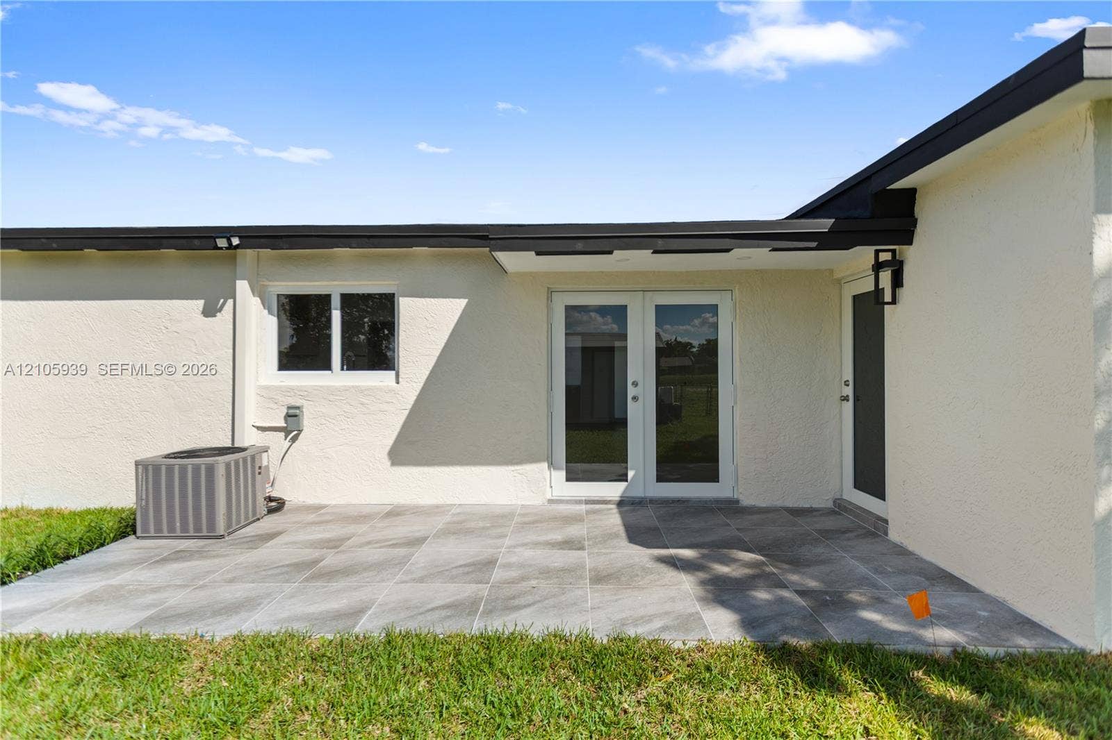 2850 NW 205th Street, Miami Gardens, FL 33056 Rear patio featuring large-format gray tile flooring, double-glass entry doors, an attached exterior light fixture, and a stucco finish