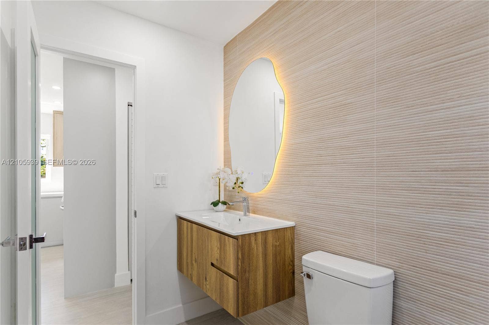 2850 NW 205th Street, Miami Gardens, FL 33056 Floating wood-finish vanity with an integrated sink, organic-shaped backlit mirror, and textured tile wall accent