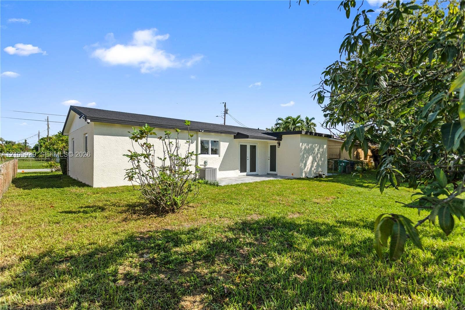 2850 NW 205th Street, Miami Gardens, FL 33056 Rear exterior featuring a smooth stucco facade, dark shingled roof, glass sliding doors, and a sprawling grass yard