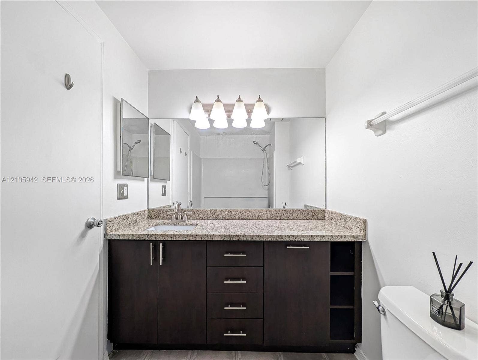 271 Duval Court, Weston, Weston, FL 33326 Bathroom vanity featuring dark-toned cabinetry with integrated shelving, stone-finish countertop, undermount sink, and four-light fixture