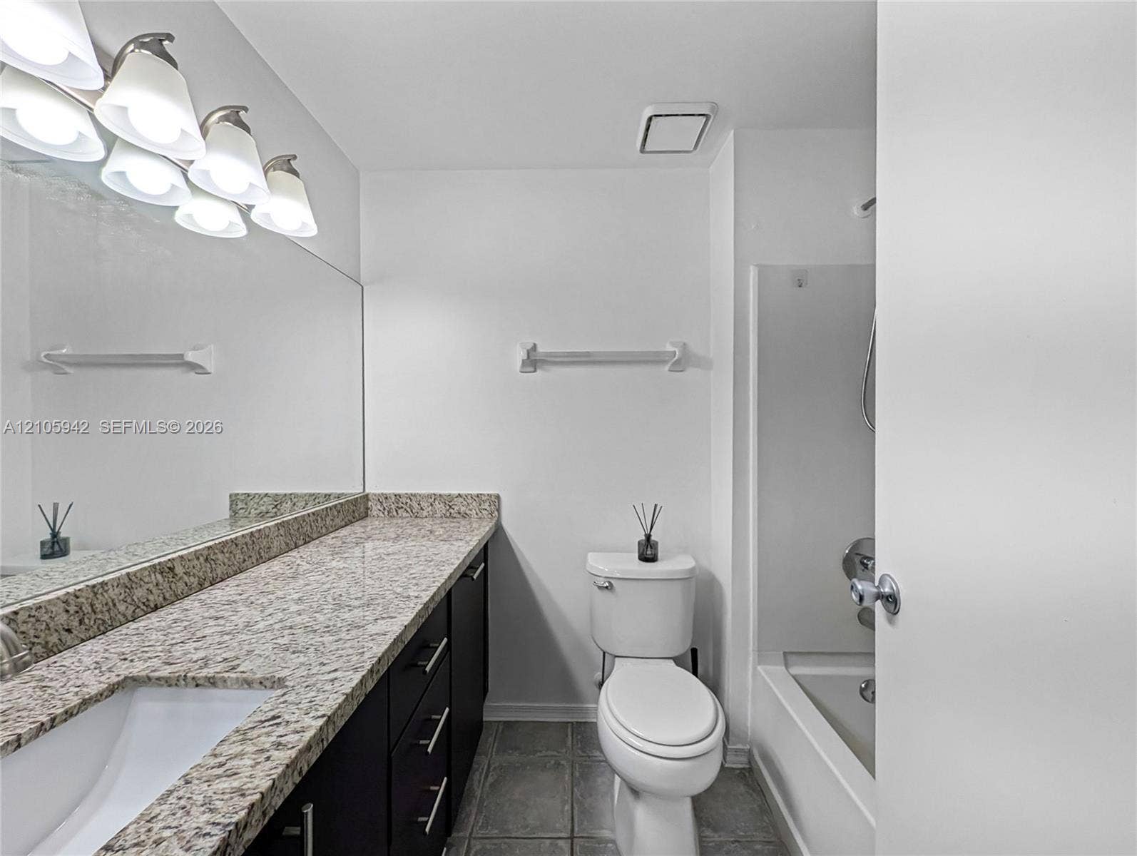 271 Duval Court, Weston, Weston, FL 33326 Full-width wall mirror, stone-composite countertop, dark-finish cabinetry, ceramic tile flooring, and a shower-tub combination