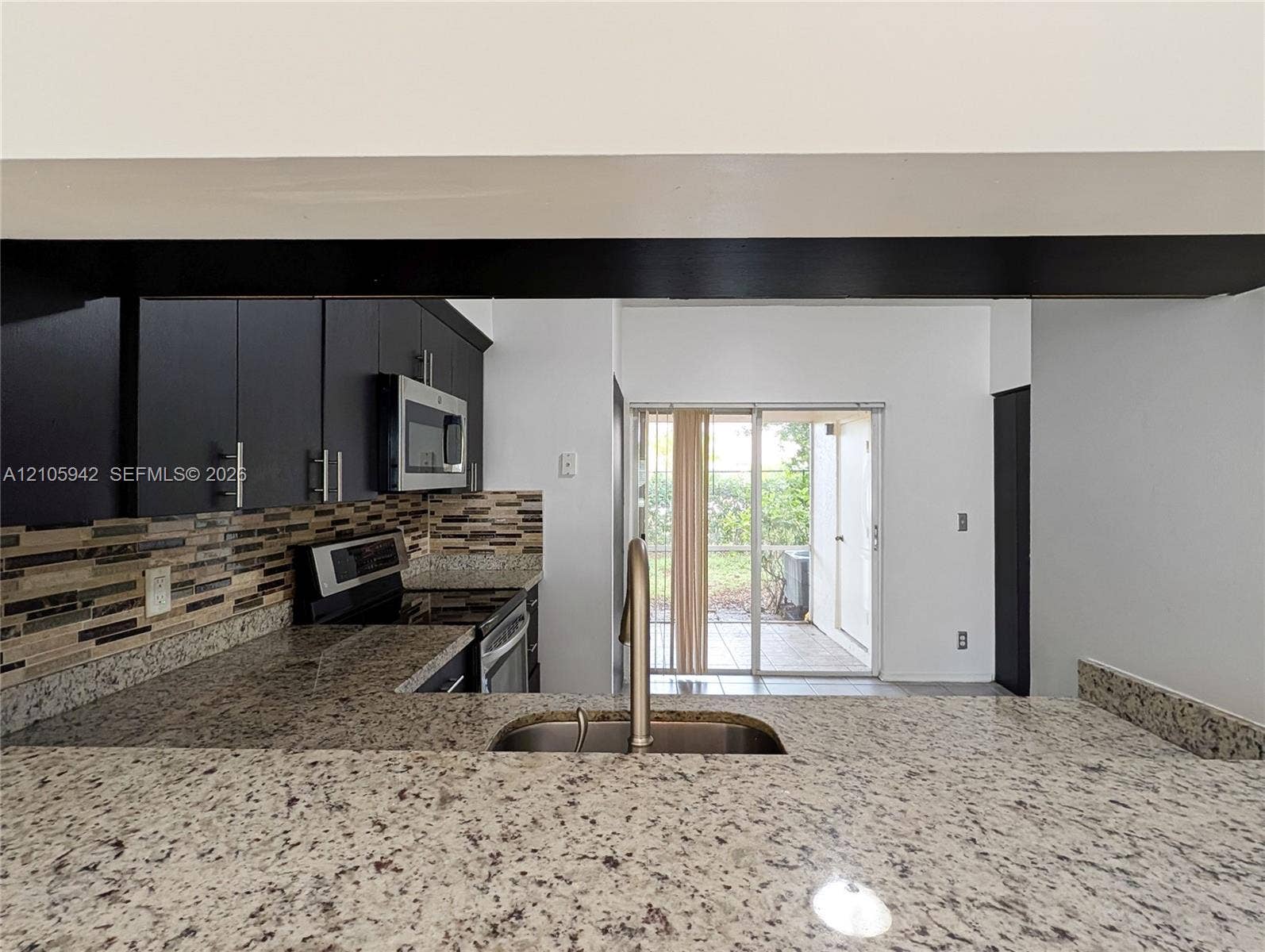 271 Duval Court, Weston, Weston, FL 33326 Kitchen featuring a stone-surface breakfast bar, mosaic tile backsplash, dark cabinetry, stainless steel microwave, and sliding glass doors