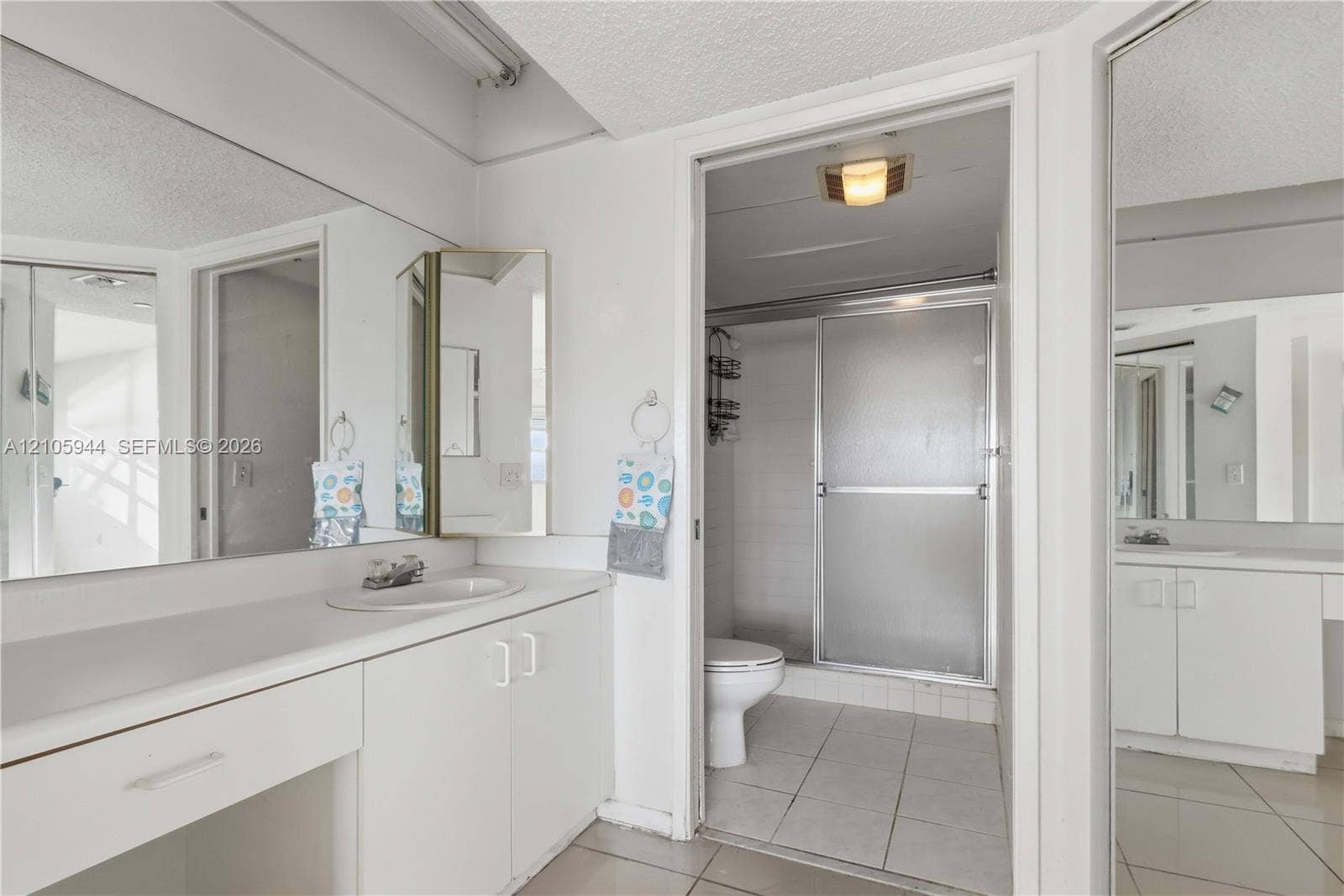 Bathroom featuring a full-width vanity with integrated basin, expansive wall-mounted mirror, white cabinetry, and a separate water closet area with a walk-in shower enclosure and tile flooring