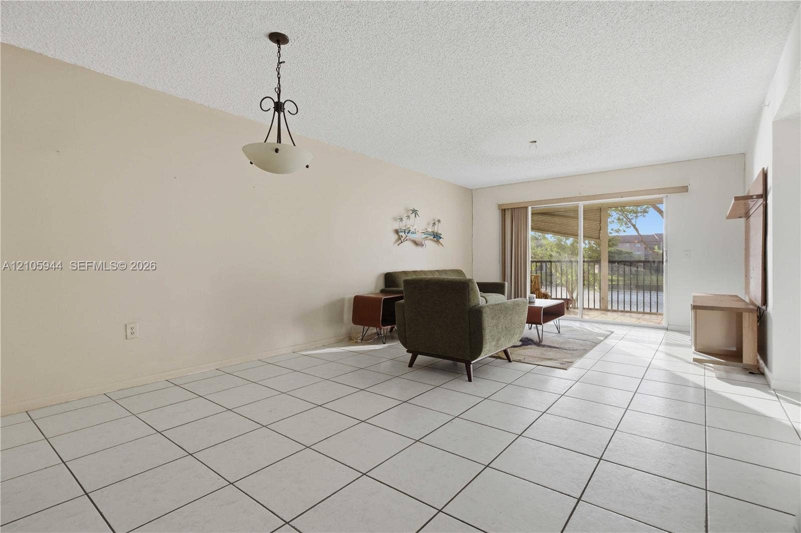 Open living area featuring large-format ceramic floor tiling, a multi-light pendant fixture, and sliding glass doors with direct access to a private balcony