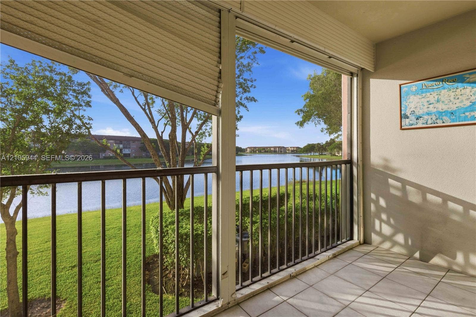 Screened-in balcony featuring tile flooring, metal railings, and retractable privacy shutters overlooking a lake and landscaped grounds