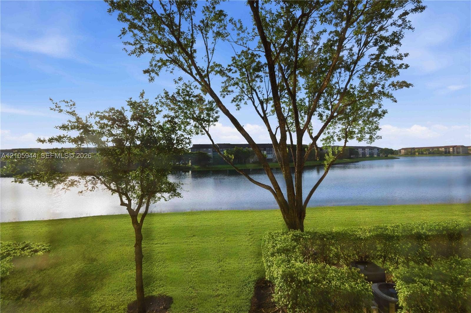 Waterfront setting featuring a grassy lawn, mature trees, and manicured shrubbery