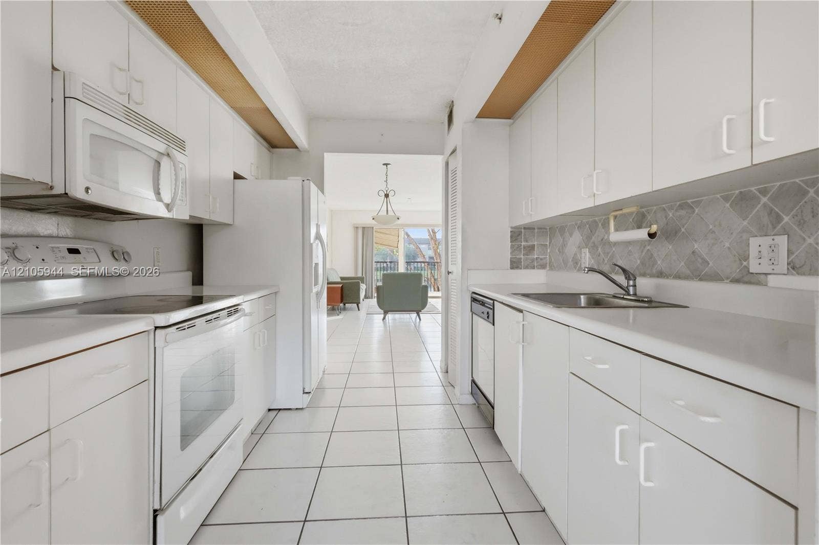 Galley kitchen featuring white cabinetry, solid-surface countertops, stone tile backsplash, integrated white appliances, and ceramic tile flooring