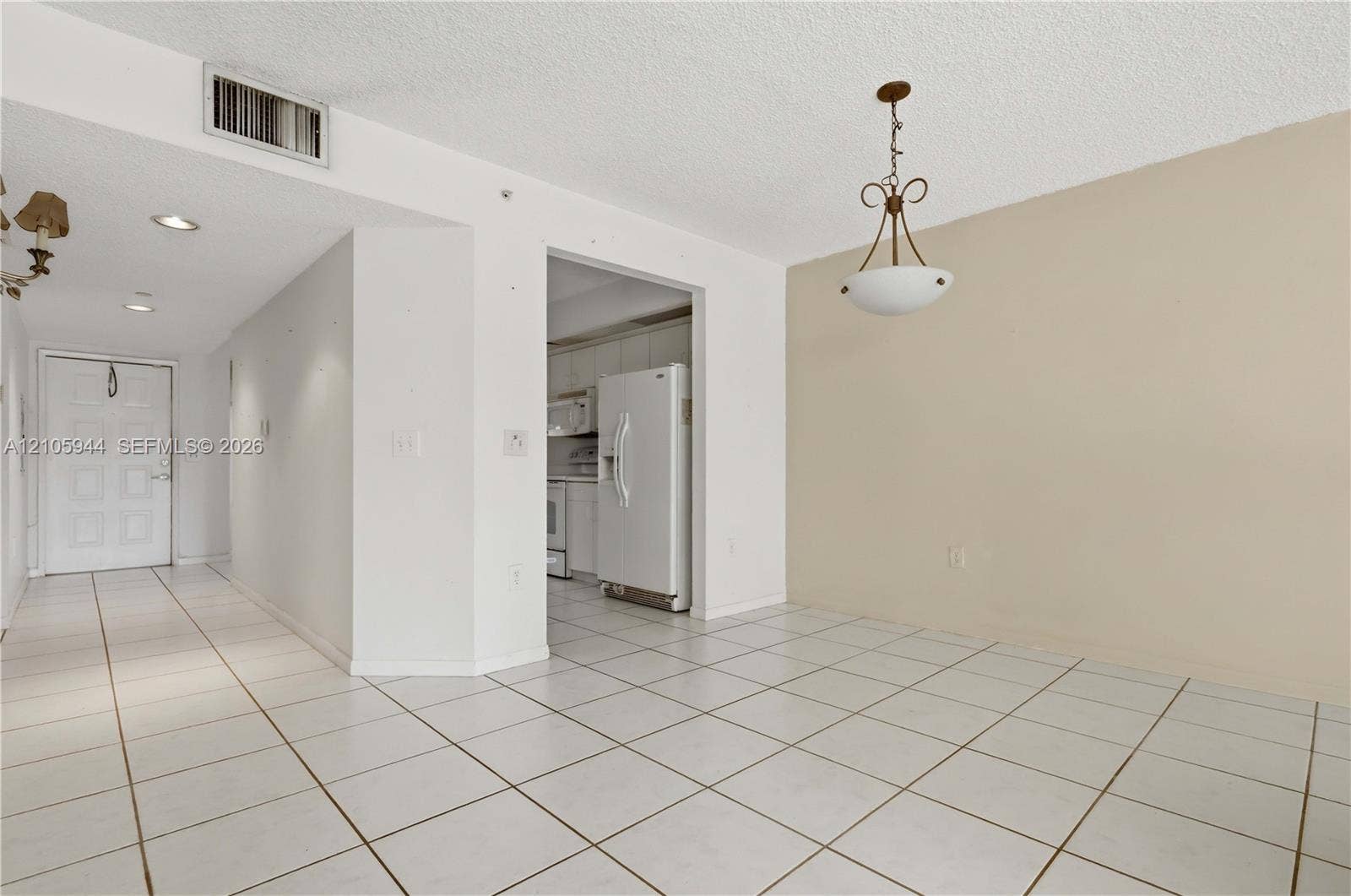 Open-concept interior featuring light-toned tile flooring, a multi-light pendant fixture, recessed ceiling lighting, and a six-panel entry door