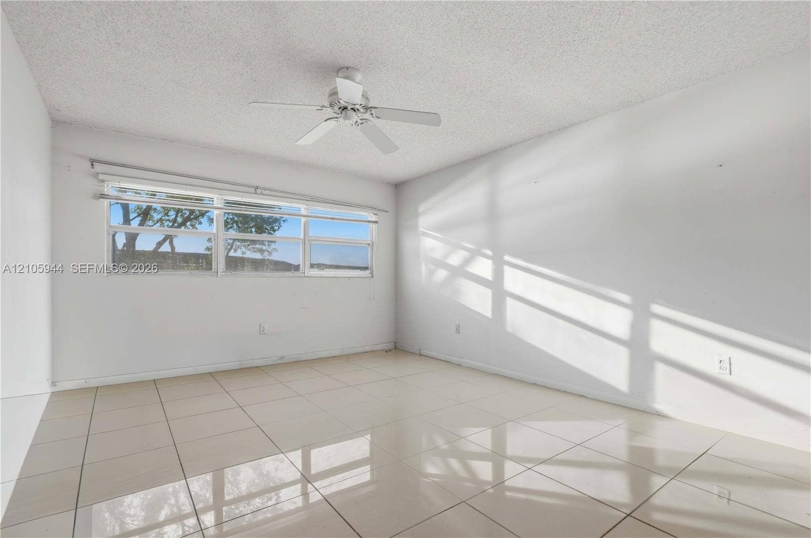 Neutral-toned interior featuring large-format polished tile flooring, white walls, and a ceiling-mounted fan with integrated lighting