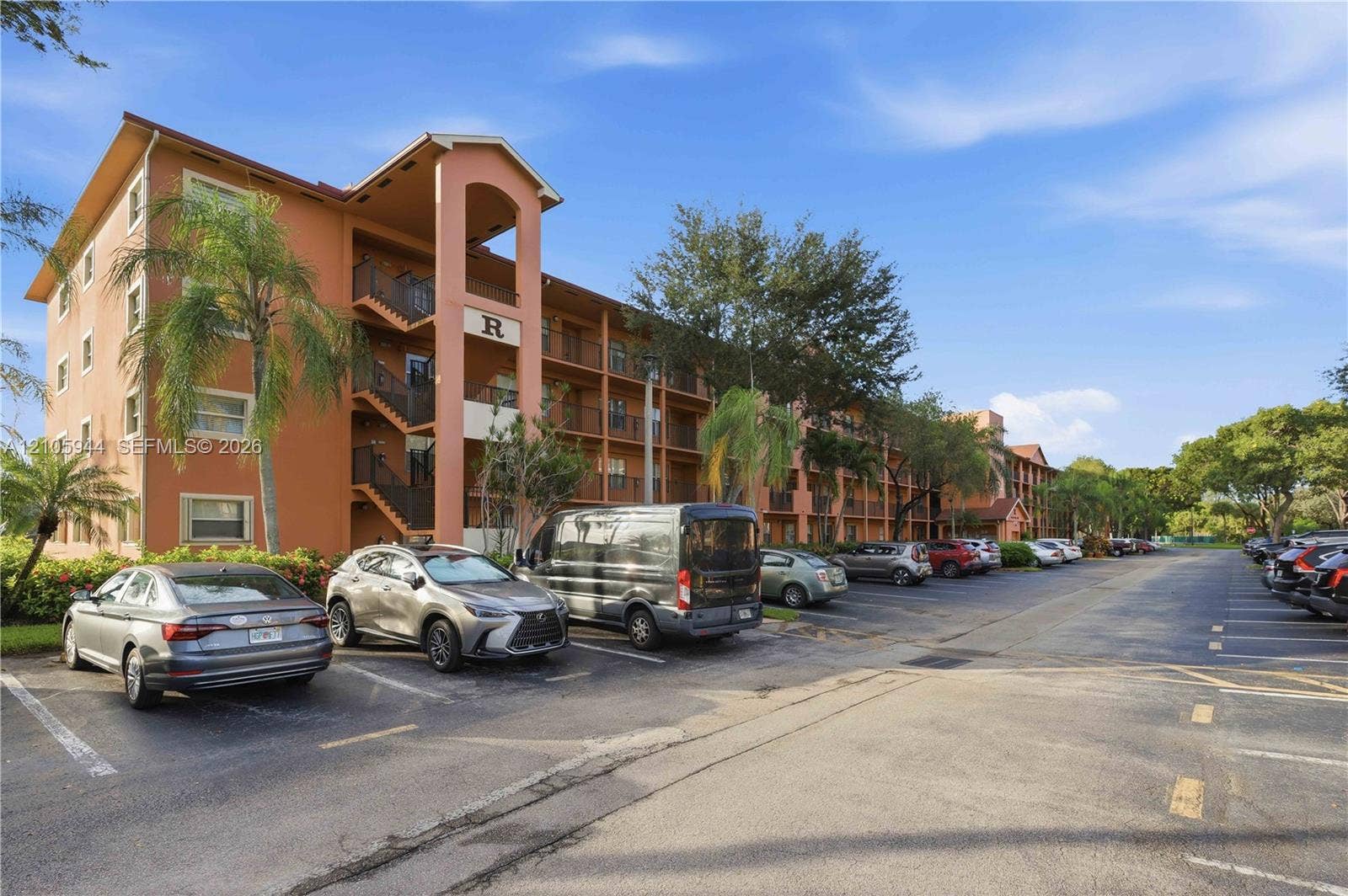 Multi-story stucco exterior featuring covered balconies, recessed stairwells, and paved surface parking