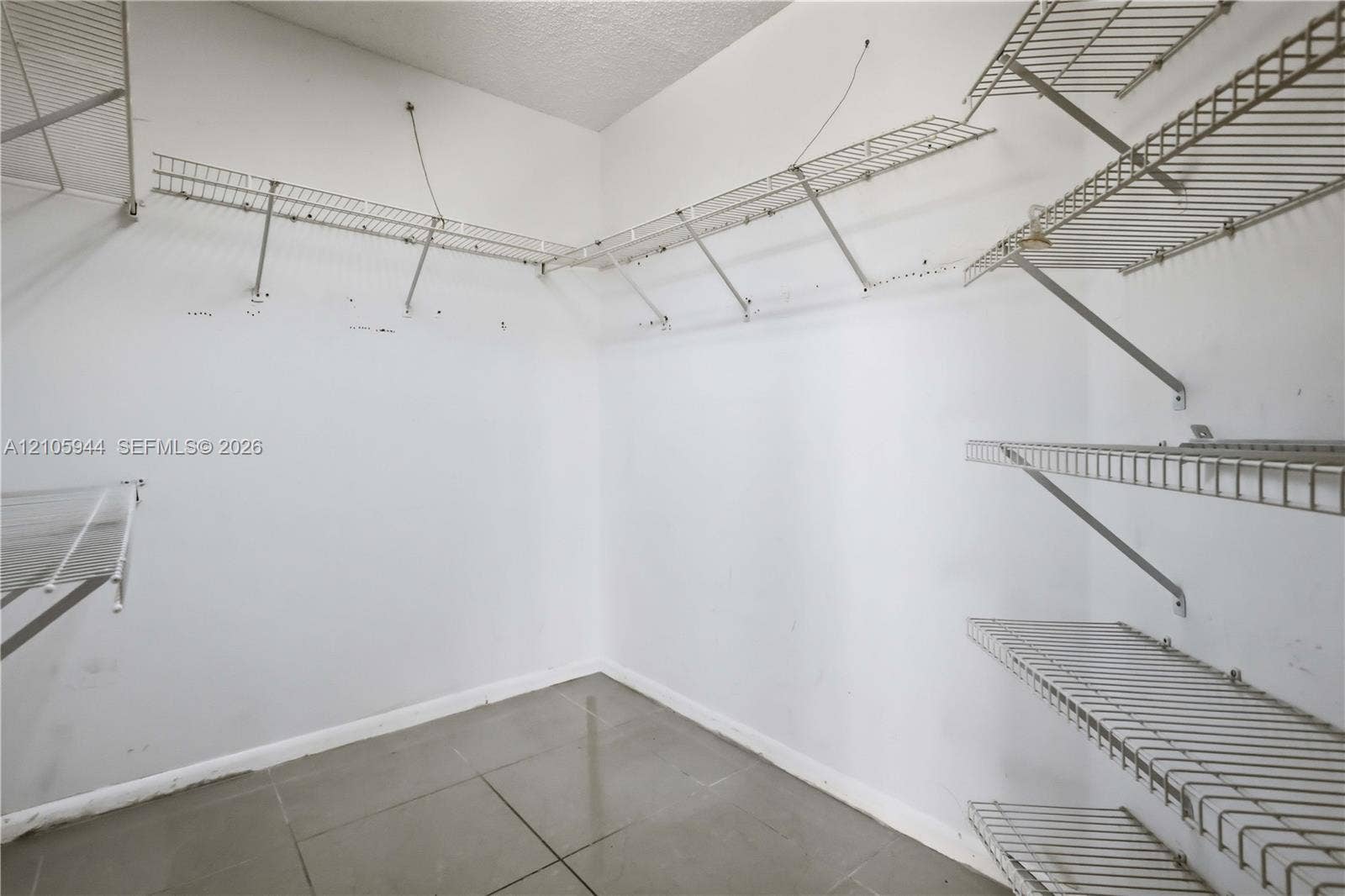 Storage space featuring white walls, neutral large-format floor tiles, and multi-tiered wall-mounted metal wire shelving