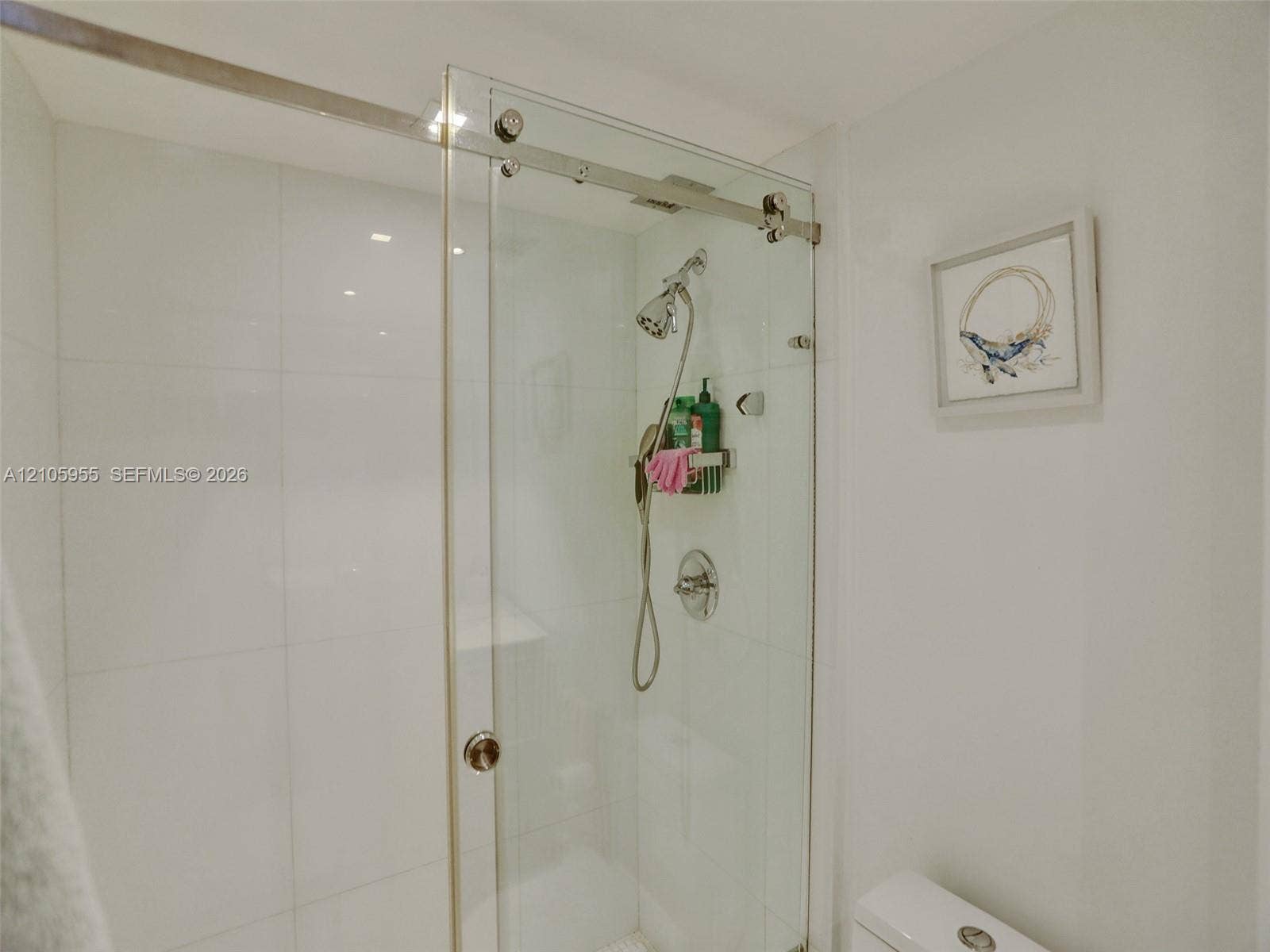 18011 Biscayne Boulevard, #1904, Aventura, FL 33160 Shower enclosure featuring a frameless glass sliding door, polished metal hardware, large-format white wall tile, and an adjustable handheld shower fixture