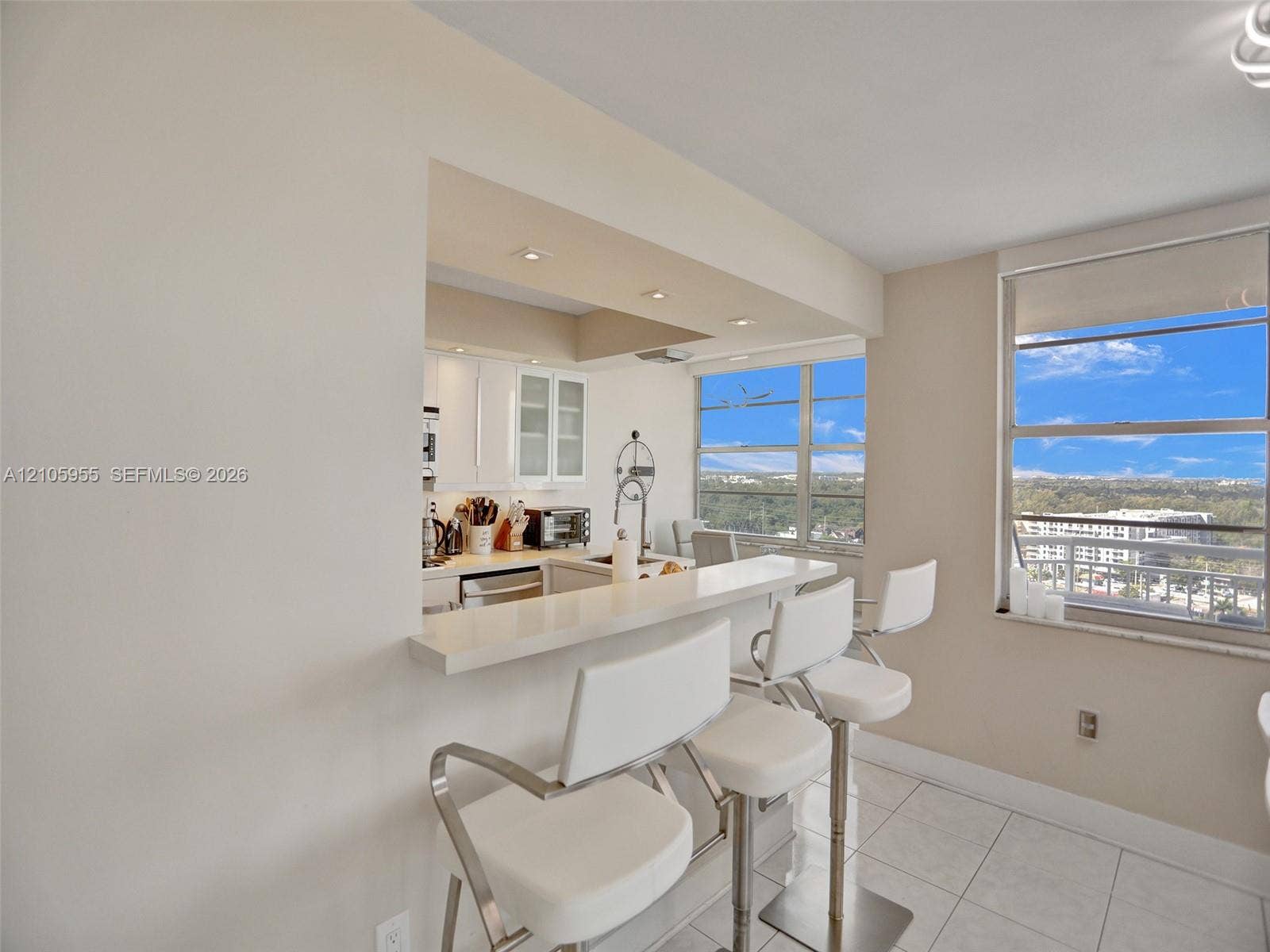 18011 Biscayne Boulevard, #1904, Aventura, FL 33160 Kitchen featuring a white quartz breakfast bar, white cabinetry with glass-front accents, recessed lighting, and large windows with exterior scenery