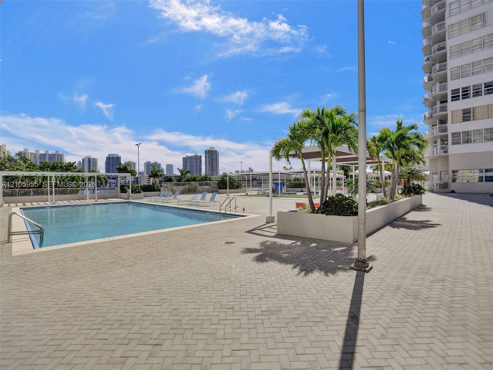 18011 Biscayne Boulevard, #1904, Aventura, FL 33160 Outdoor swimming pool featuring a paved deck, built-in planter beds with mature palm trees, metal shade structures, and metal pool entry rails