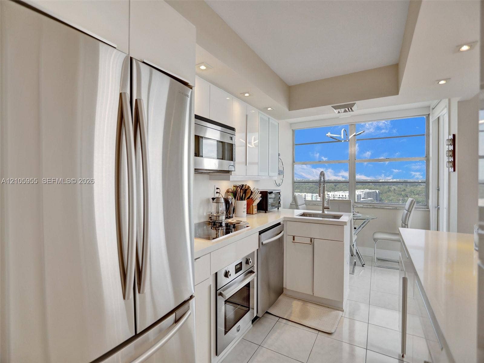 18011 Biscayne Boulevard, #1904, Aventura, FL 33160 Kitchen featuring high-gloss white cabinetry, stainless steel appliances, solid surface countertops, tile flooring, and large floor-to-ceiling windows