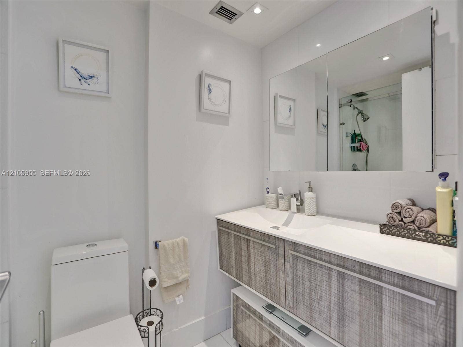 18011 Biscayne Boulevard, #1904, Aventura, FL 33160 Floating vanity with wood-finish cabinetry, integrated dual-basin sink, oversized frameless mirror, and glass-enclosed shower