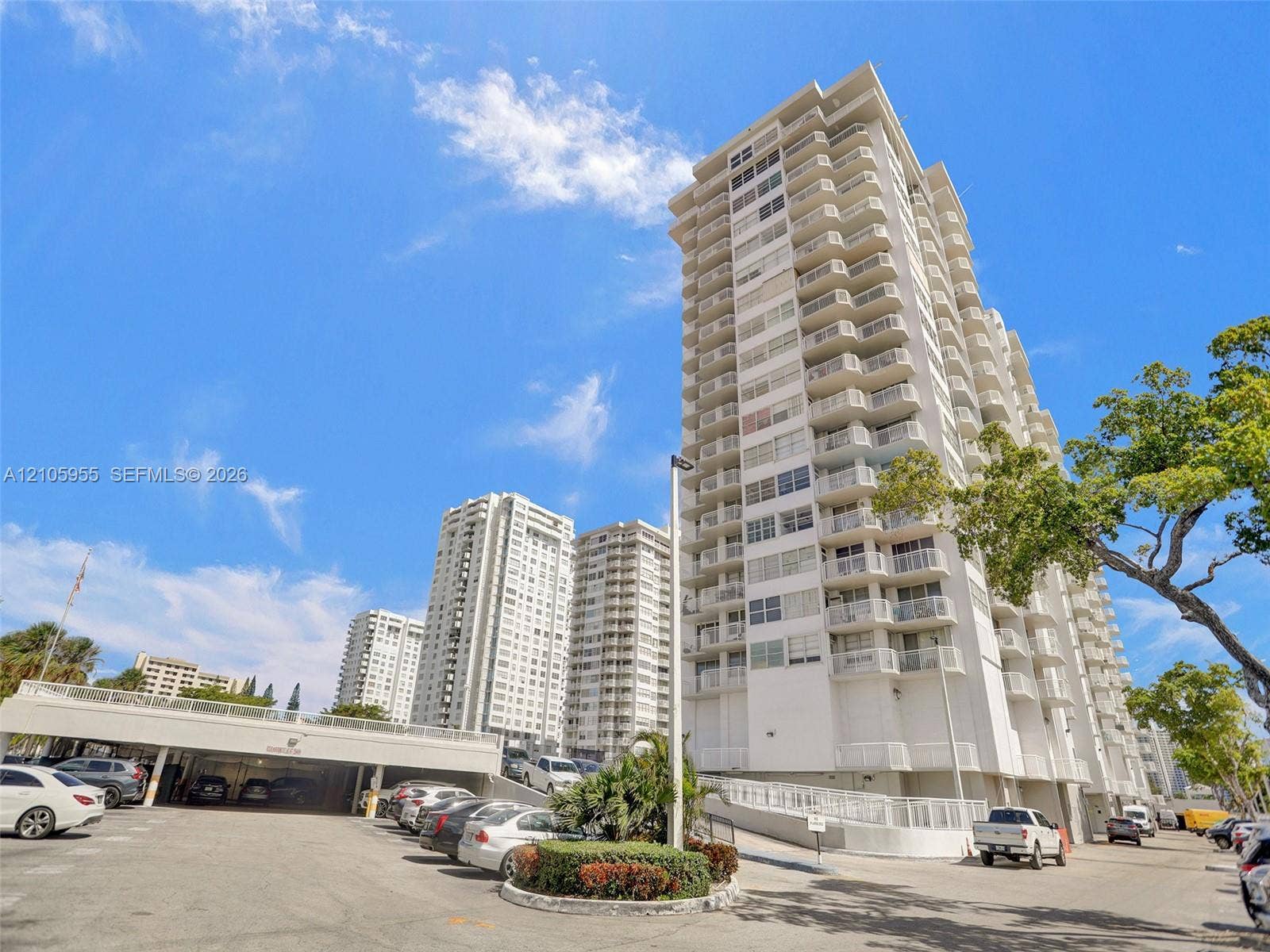 18011 Biscayne Boulevard, #1904, Aventura, FL 33160 High-rise residential exterior featuring stacked private balconies, concrete facade, and integrated covered parking structure with landscaping