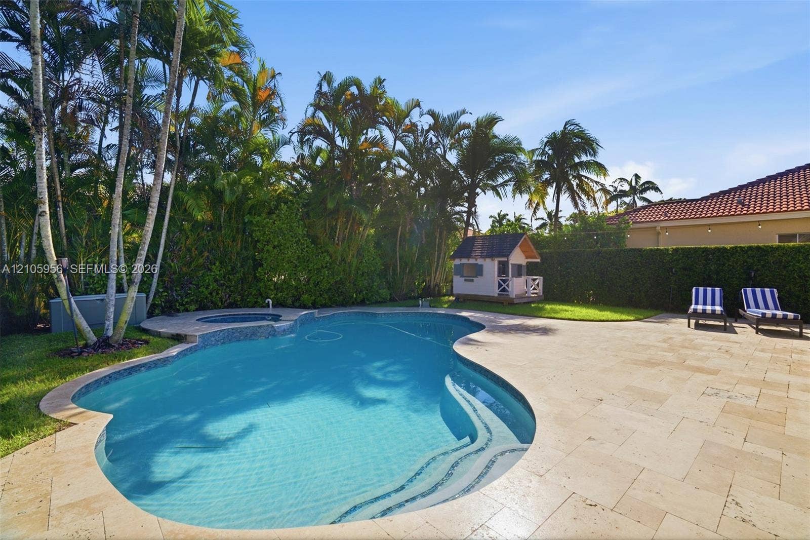 1154 Croton Court, Weston, Weston, FL 33327 Free-form swimming pool featuring an integrated spillover spa, wide stone-paver decking, mature perimeter palm trees, and an enclosed lawn