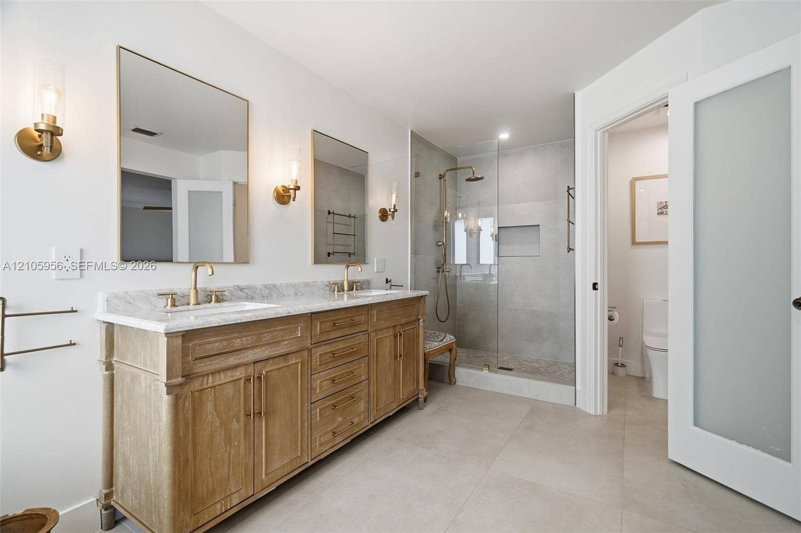 1154 Croton Court, Weston, Weston, FL 33327 Dual-sink vanity with stone countertop, walk-in glass-enclosed shower featuring gold-tone hardware, wall-mounted light fixtures, and frosted glass door