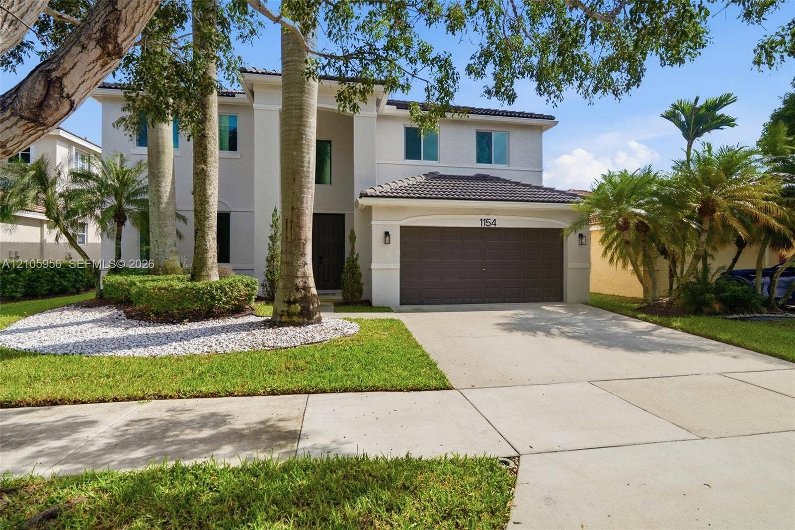 1154 Croton Court, Weston, Weston, FL 33327 Two-story residence featuring a light-toned exterior, concrete tile roof, multi-car garage, and landscaped front grounds with mature palm trees