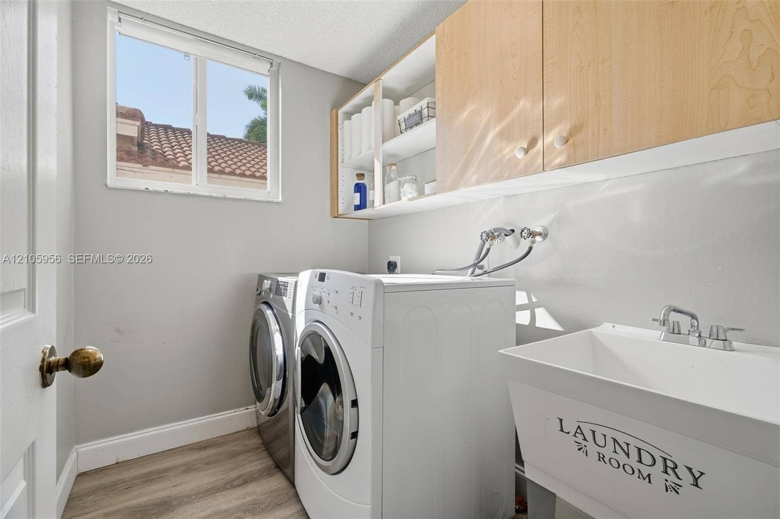 1154 Croton Court, Weston, Weston, FL 33327 Laundry area featuring light wood-finish cabinetry, built-in shelving, a utility sink with a chrome faucet, and wood-finish flooring